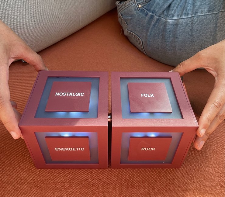 Two hands holding the two Cubit cubes together, with faces labelled Nostalgic, Folk, Energetic and Rock